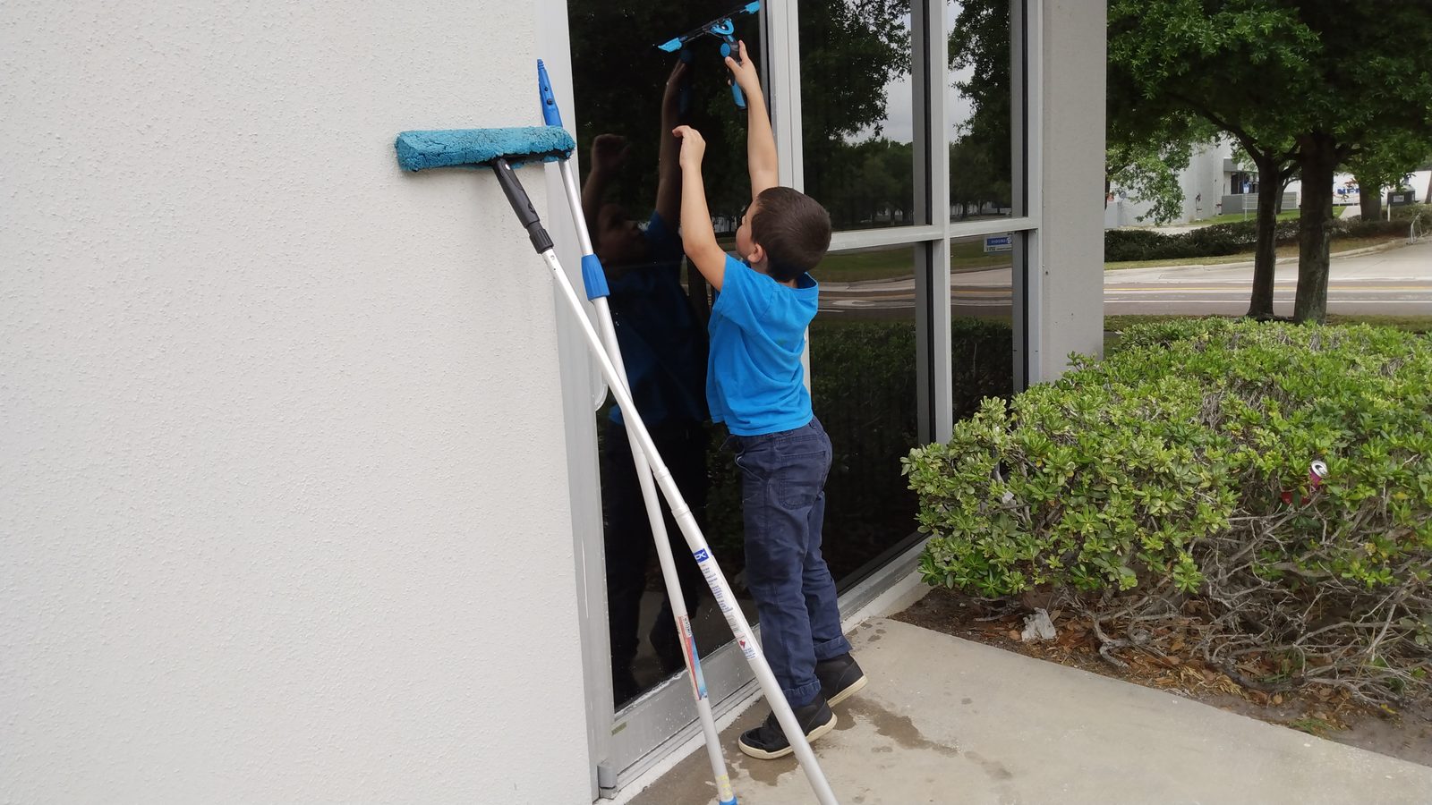 A young SqueegeeCo helper reaching up to clean commercial glass